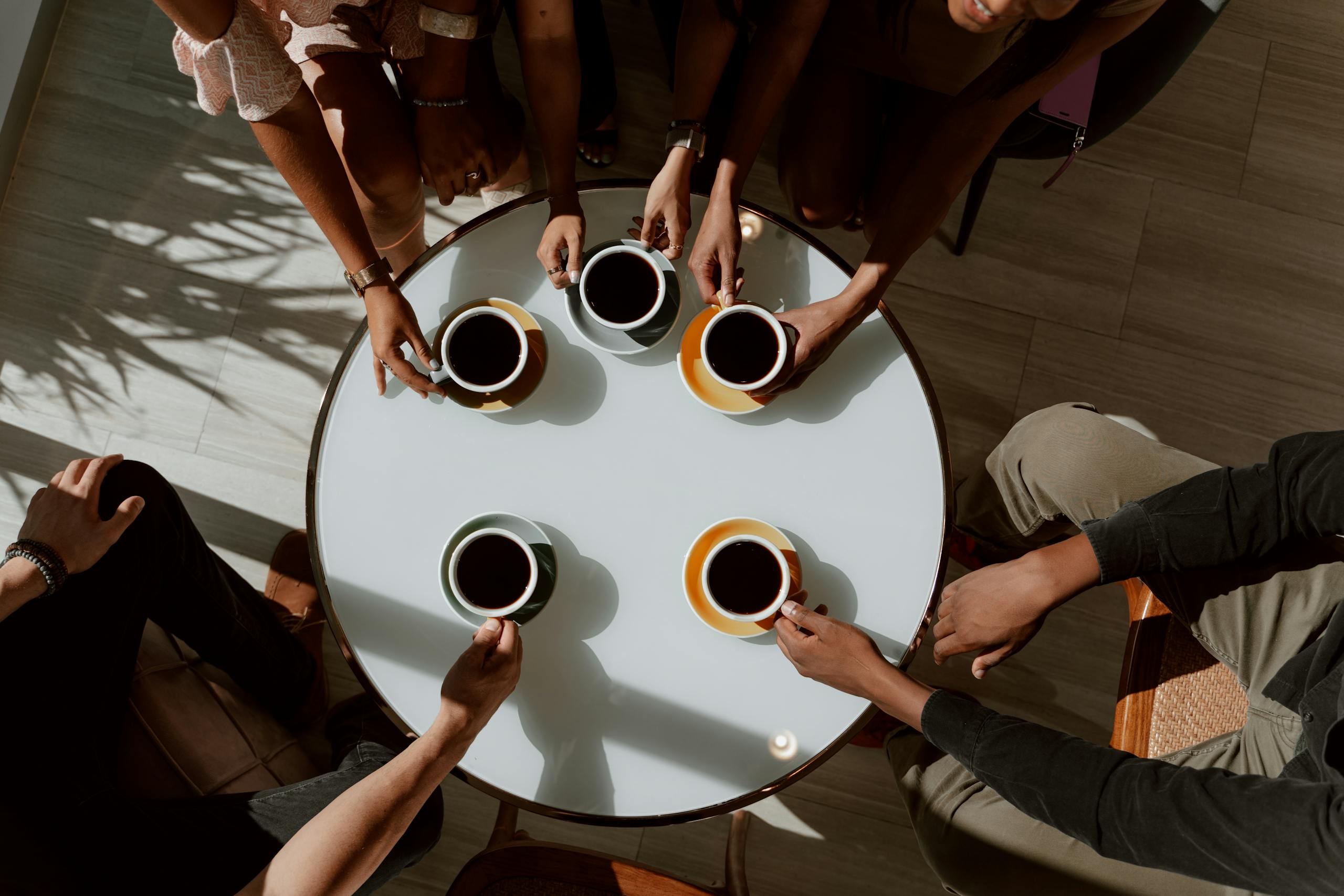 A group of friends enjoying coffee around a café table in a warm setting.